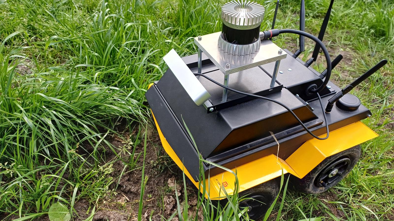 Clearpath Jackal robot from the University of Lübeck, fitted with a sensor mast and antennas, driving through grass on a pasture.
